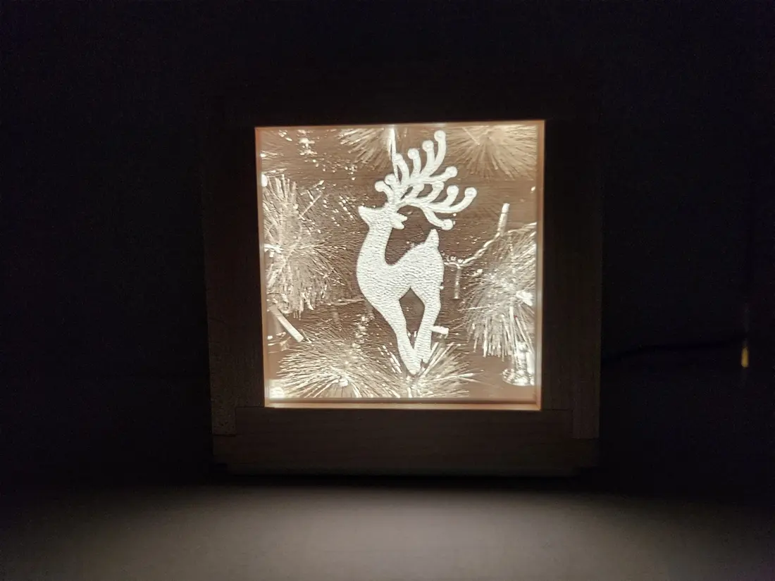 A 3D-printed lithophane of a reindeer, lit from behind in a wood frame